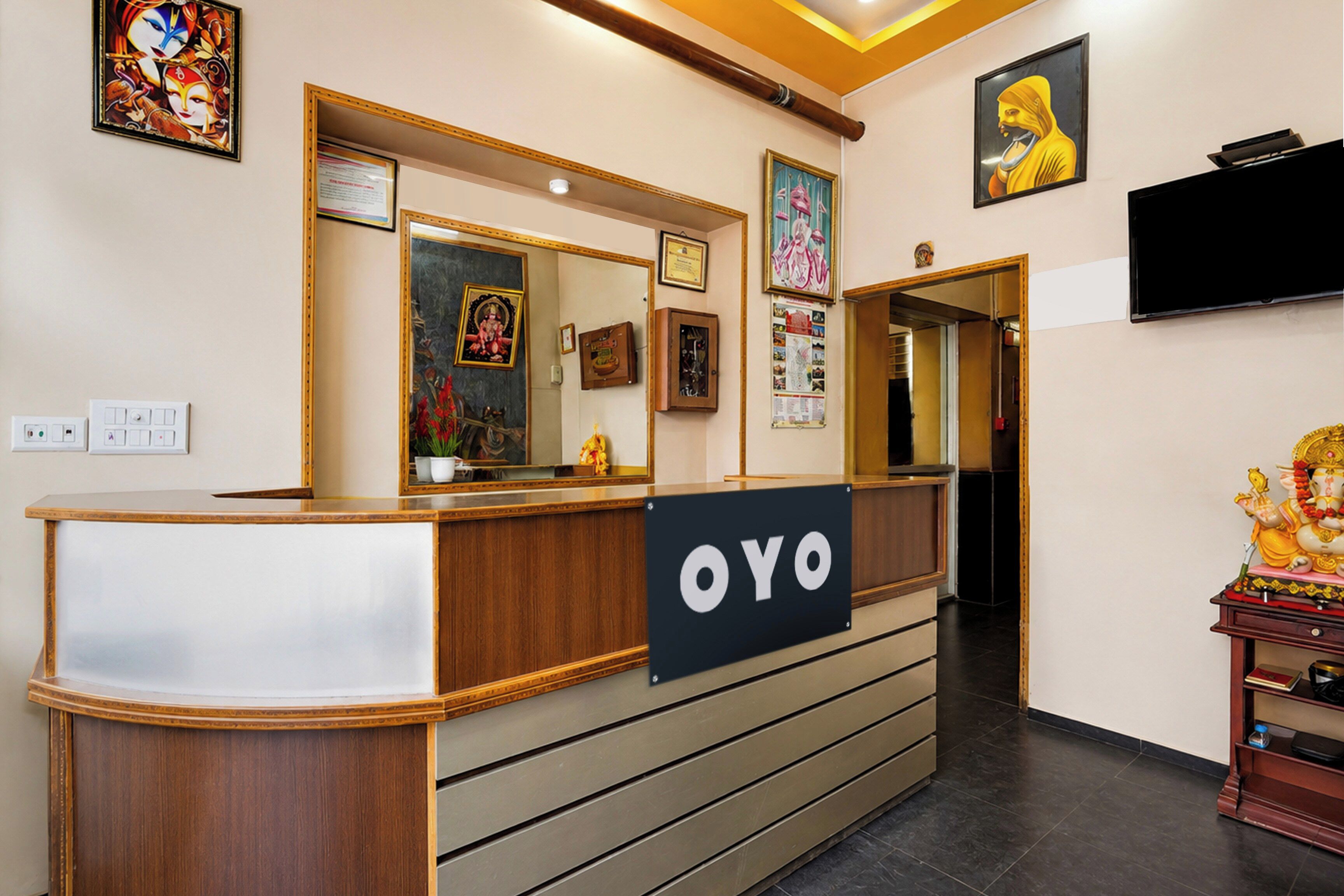 Una recepción con un cartel que dice 'OYO' en el vestíbulo de un hotel, con un espejo, obras de arte enmarcadas y un televisor montado en la pared.