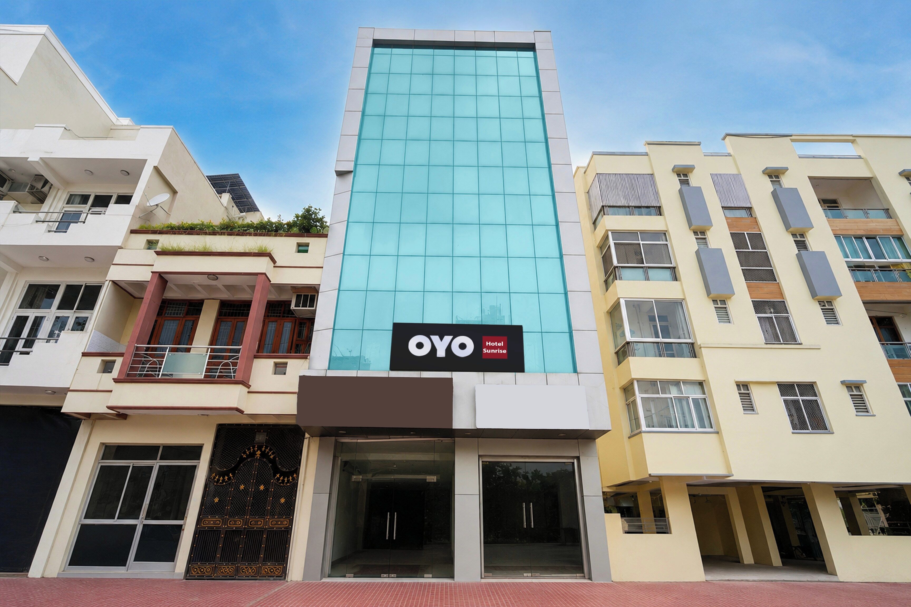 A hotel building with a modern glass facade, a sign for 'OYO Hotel Sunrise,' and a ground-level entrance with a glass door.