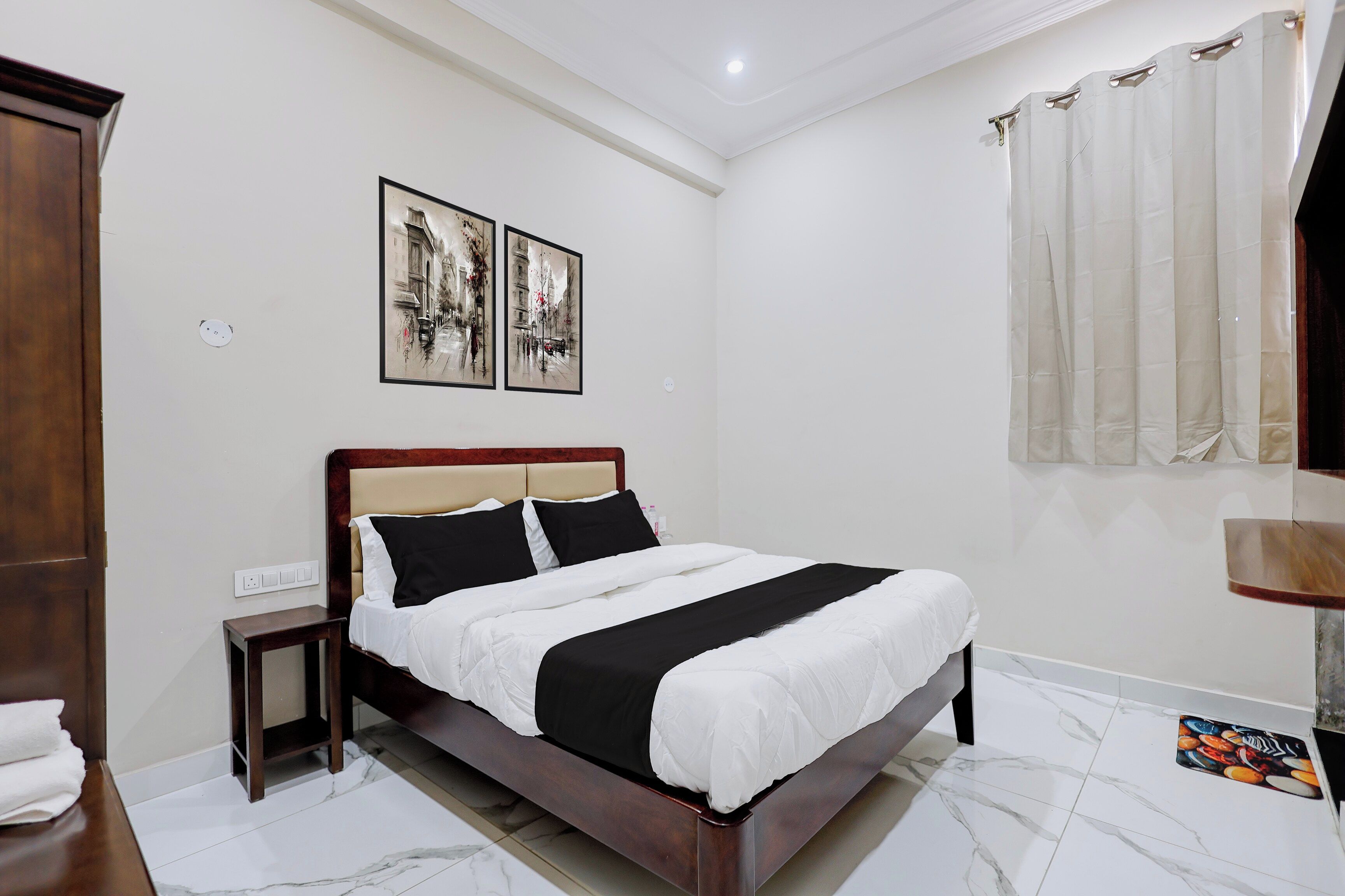 Une chambre d’hôtel avec un lit, une table de chevet, une lampe fixée au mur et une fenêtre avec des rideaux.