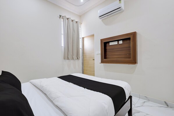 A bedroom with a bed, an air conditioner, a window with curtains, and a wooden panel on the wall.