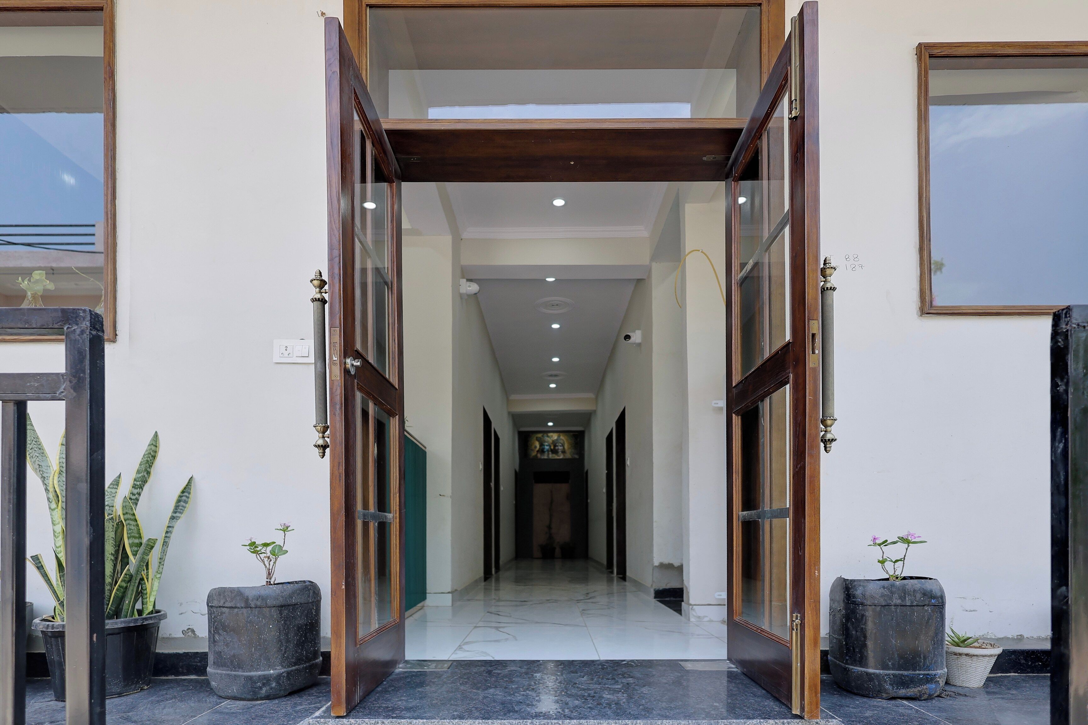 Entrada de hotel com porta grande, piso de azulejos e plantas em vasos de ambos os lados.