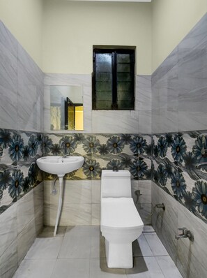 Ein Badezimmer mit weißem Waschbecken, WC und Bidet, mit Wandfliesen in einem Blumenmuster und einem kleinen Fenster über dem WC.