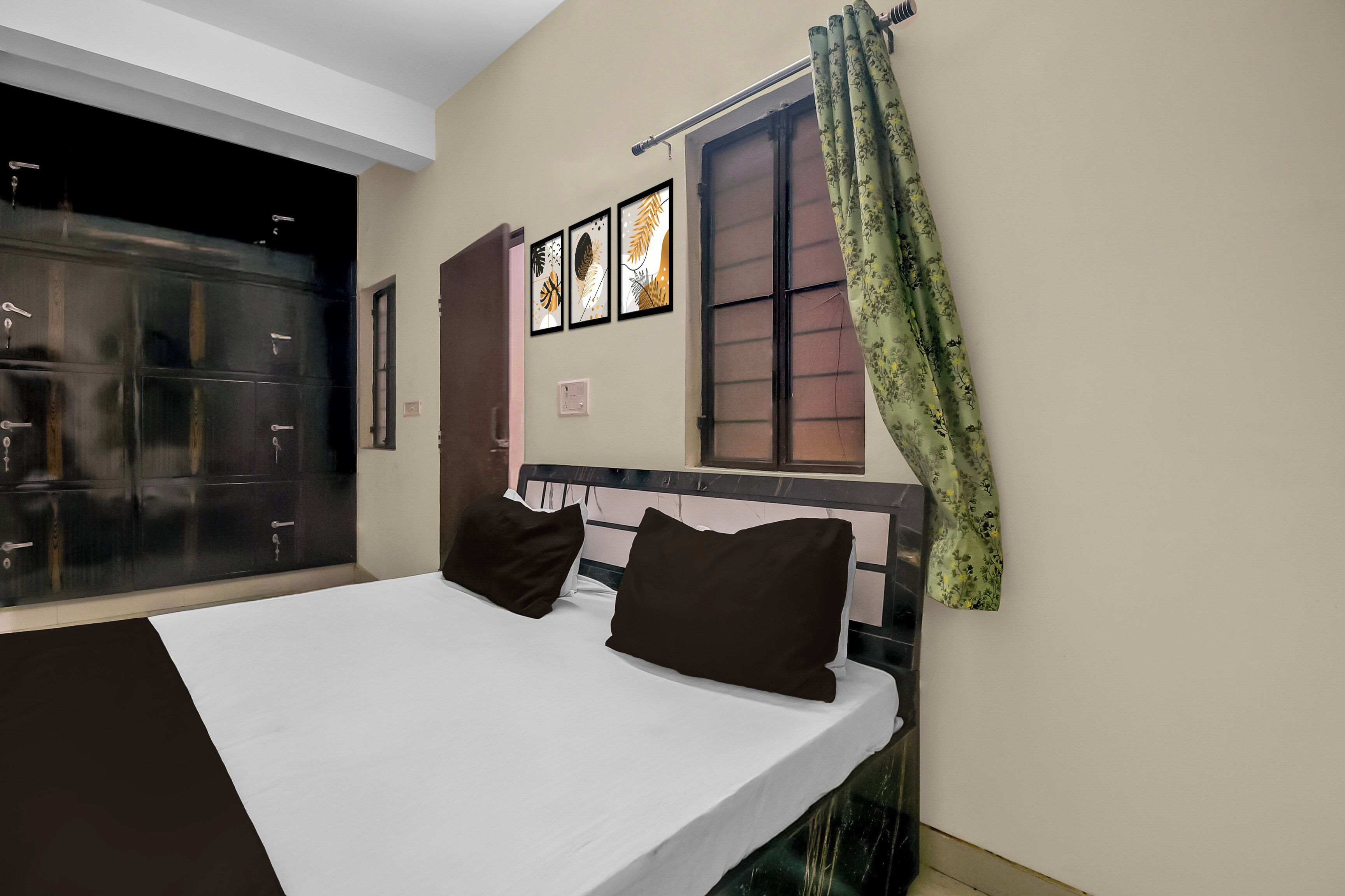 Une chambre à coucher comprenant un lit, une armoire, une fenêtre avec des rideaux et des œuvres d’art murales.