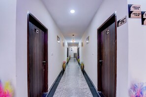 Un pasillo de hotel con puertas numeradas del 001 al 004, señales de registro de entrada y salida, y cuadros en las paredes.