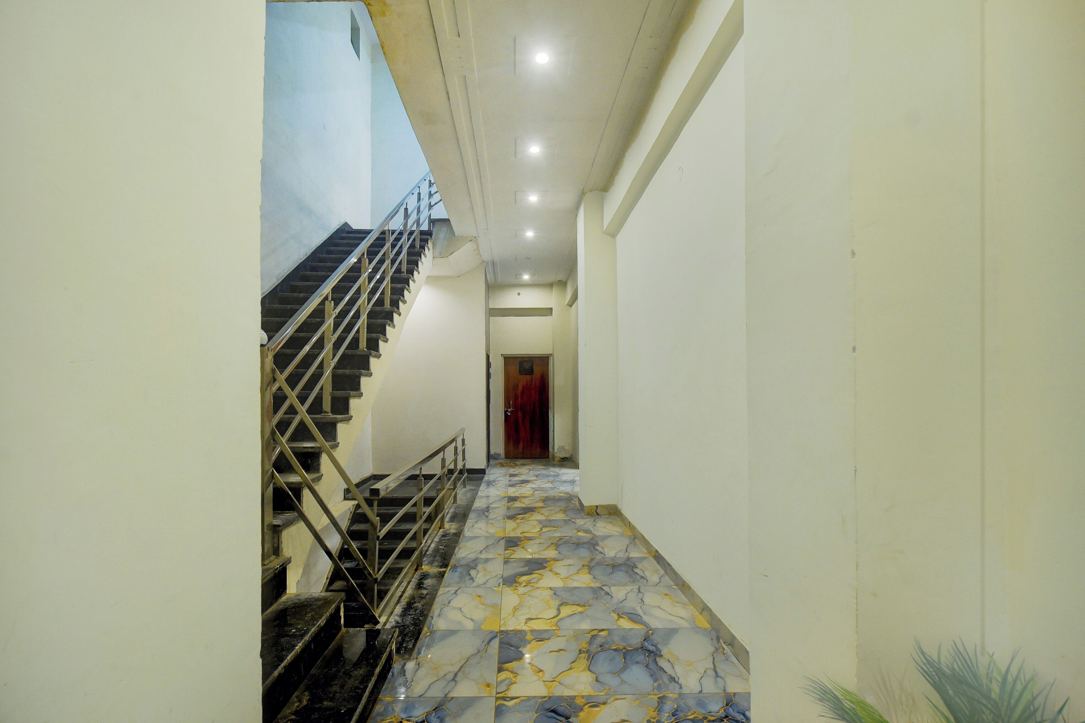 Un pasillo con piso de mármol que conduce a una escalera con barandillas de metal.