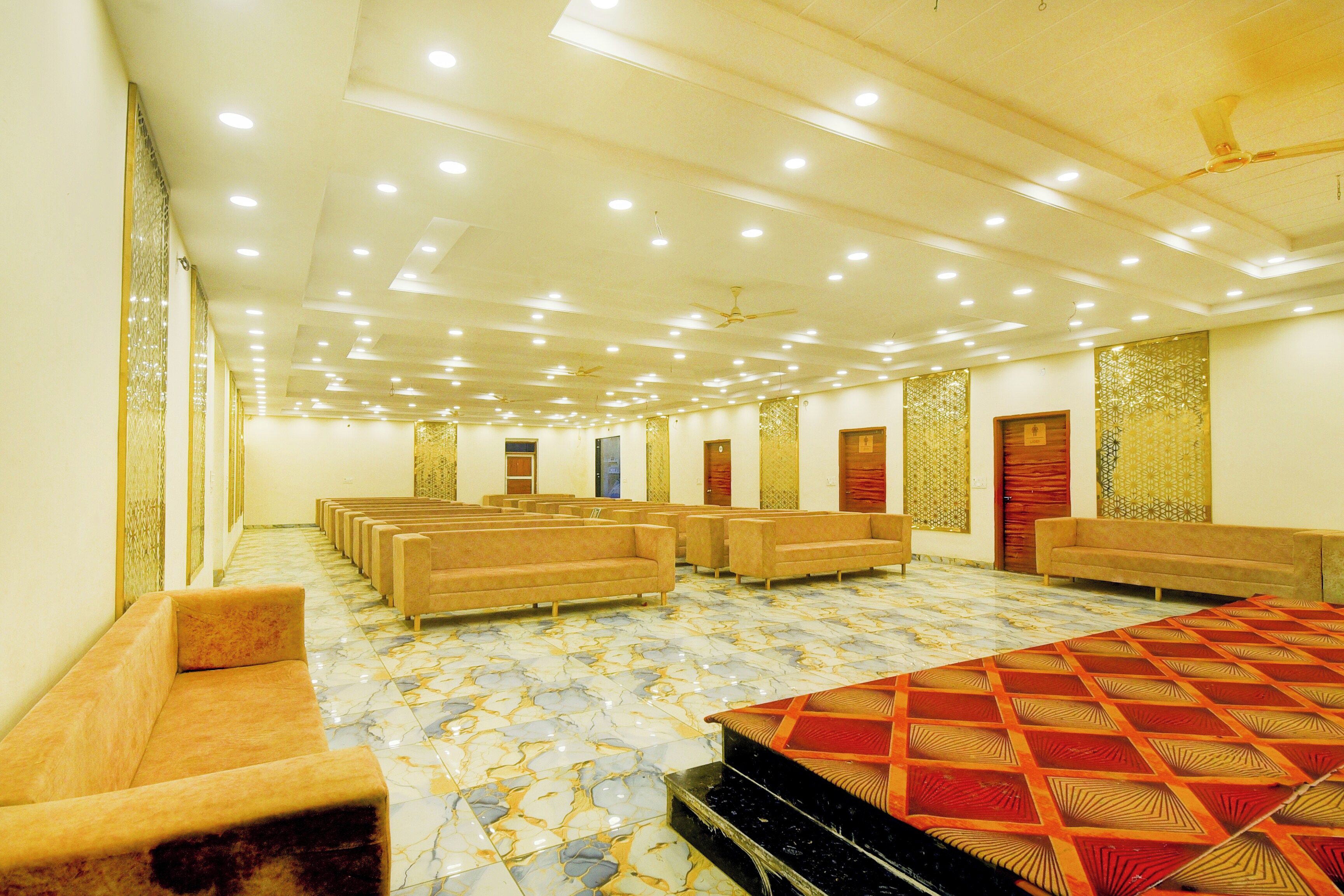 Un salón de conferencias con filas de sillas, un escenario con alfombra estampada e iluminación empotrada en el techo.