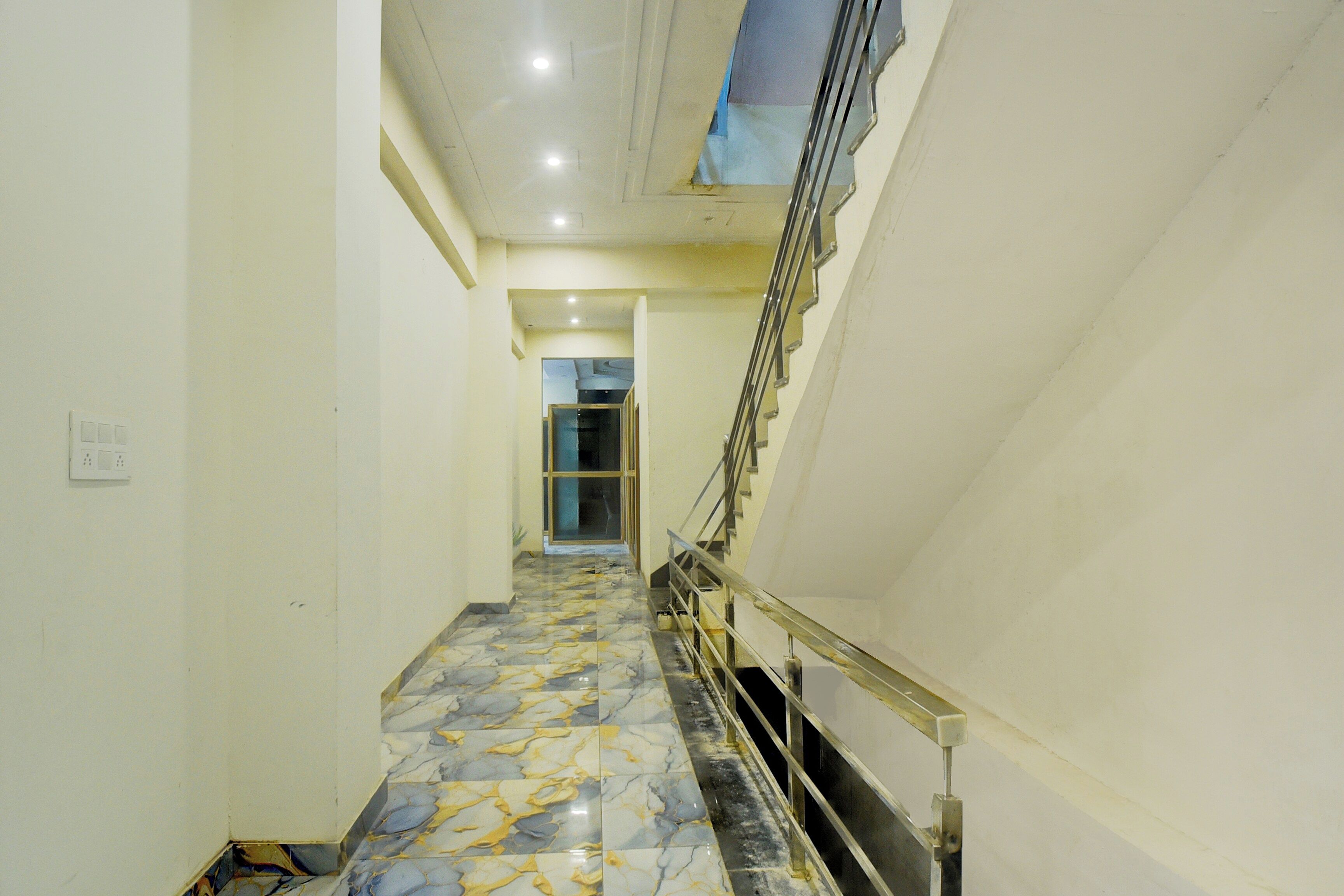 A hallway with a marble floor, a staircase on the right, and a door at the end.