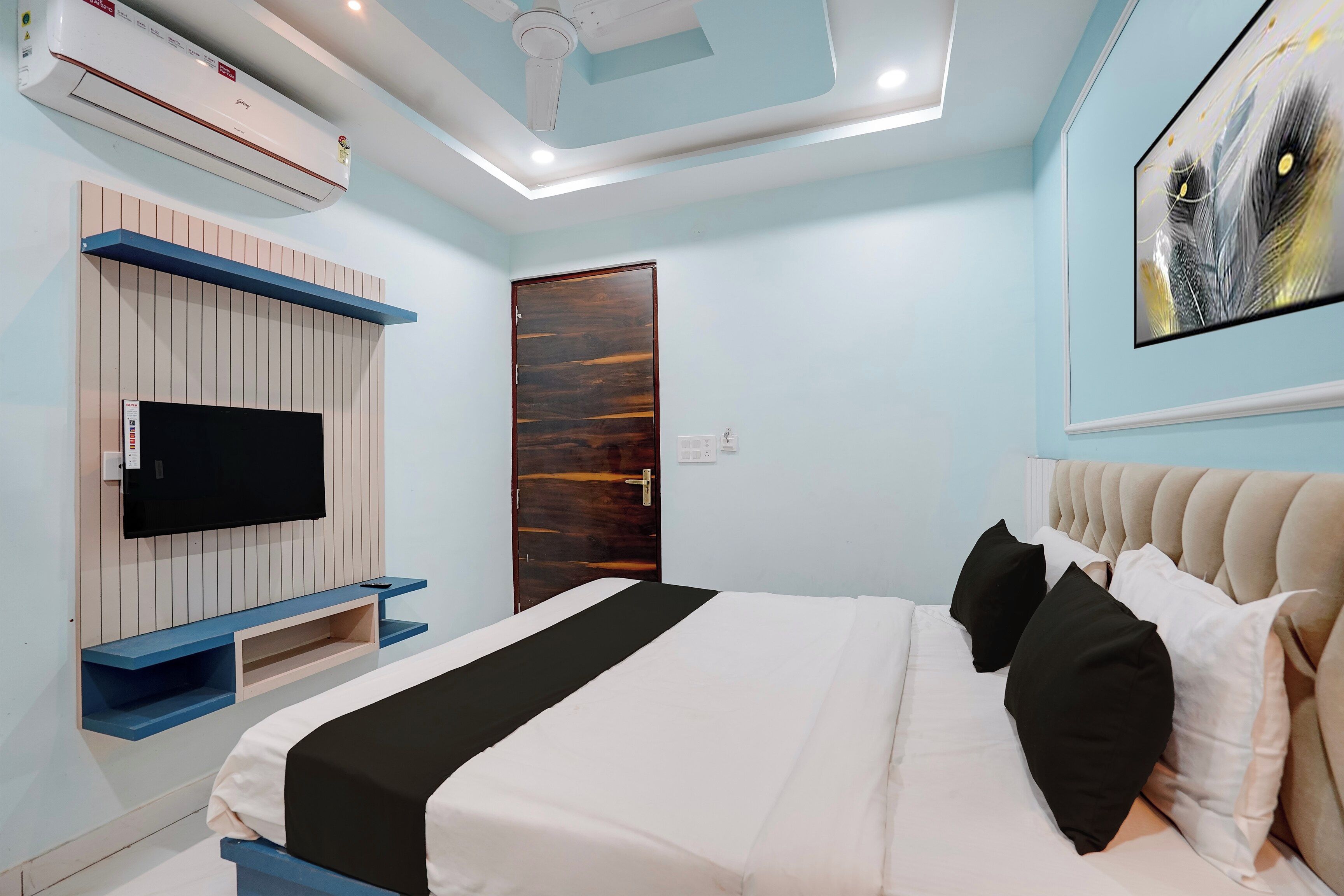 Een slaapkamer met een bed, een aan de muur bevestigde televisie, een plafondventilator en een deur.