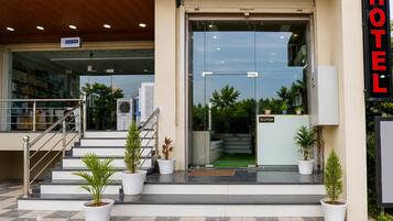 A hotel entrance with a reception desk, a staircase leading to the entrance, and potted plants.
