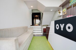 A reception area with a sofa, a staircase, and a sign that reads 'OYO'. - Hotel O Sanraj Hotel (Jaipur)