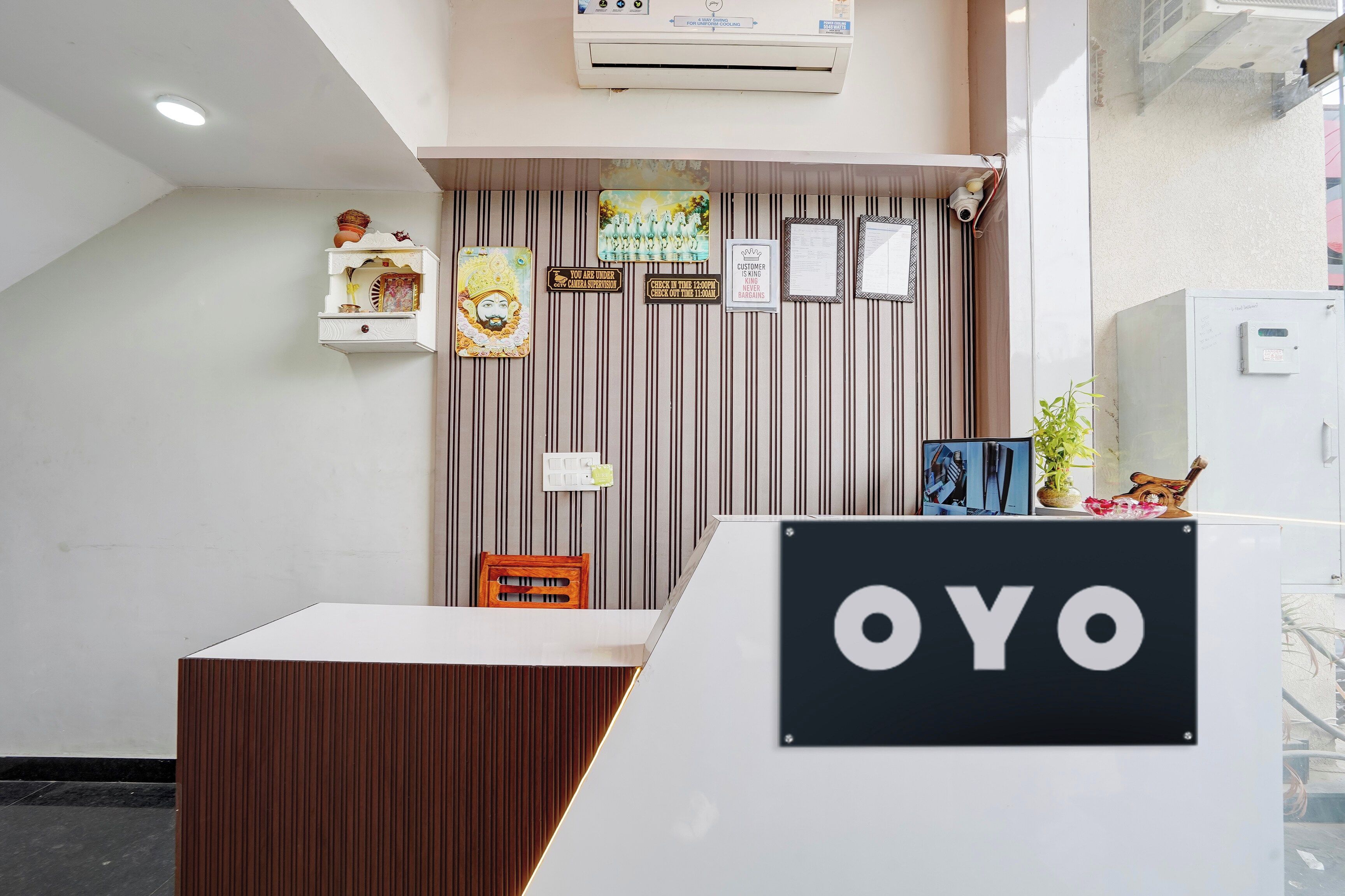 A reception desk with a sign that reads 'OYO' and a wall with vertical lines and various signs, including one that says 'CUSTOMER IS KING NEVER BARGAINS.'