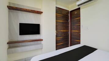 A bedroom with a bed, a mounted television, a wardrobe, and an air conditioning unit.