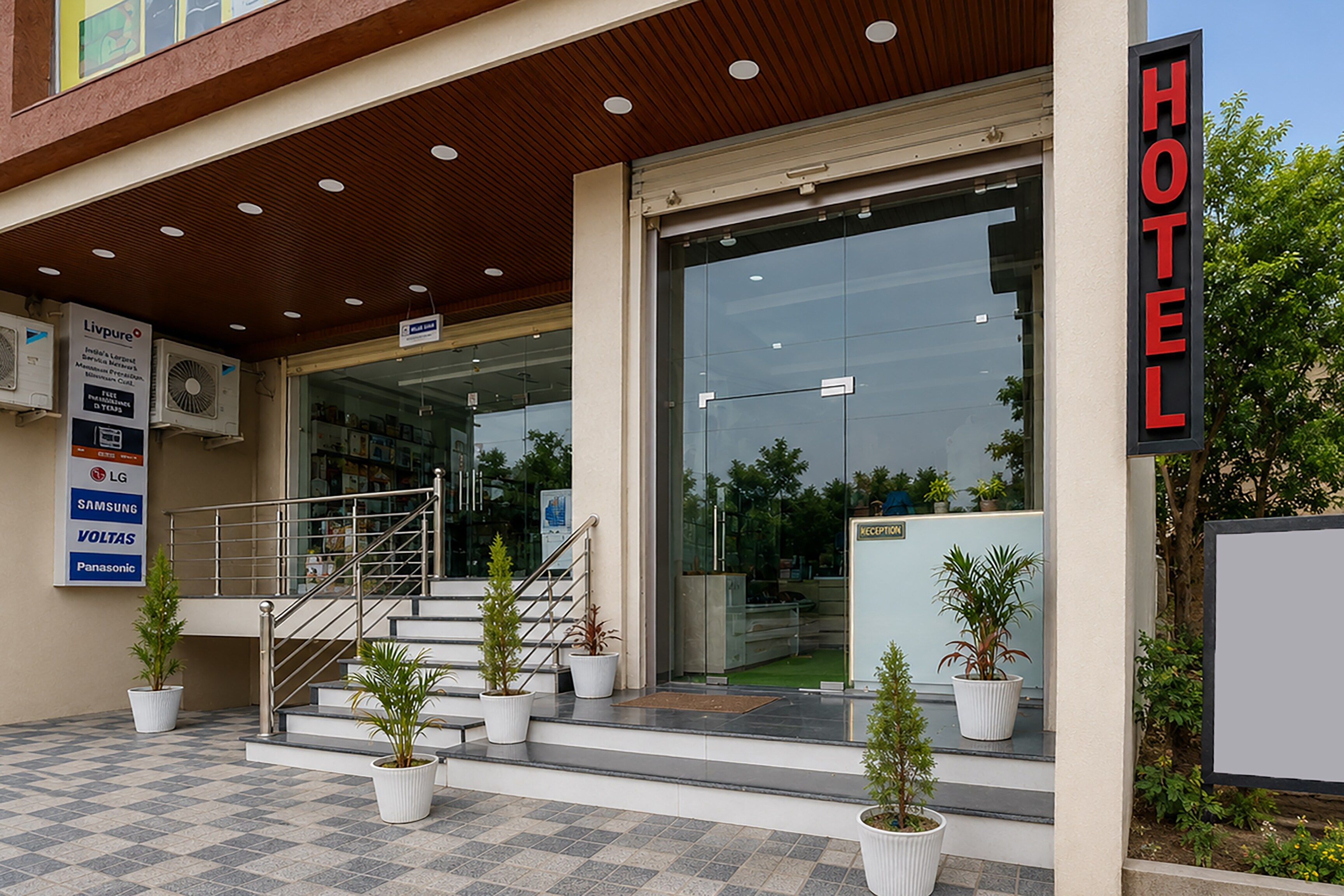 Entrada de un hotel con una escalera que lleva a la puerta, un mostrador de recepción y plantas en macetas.