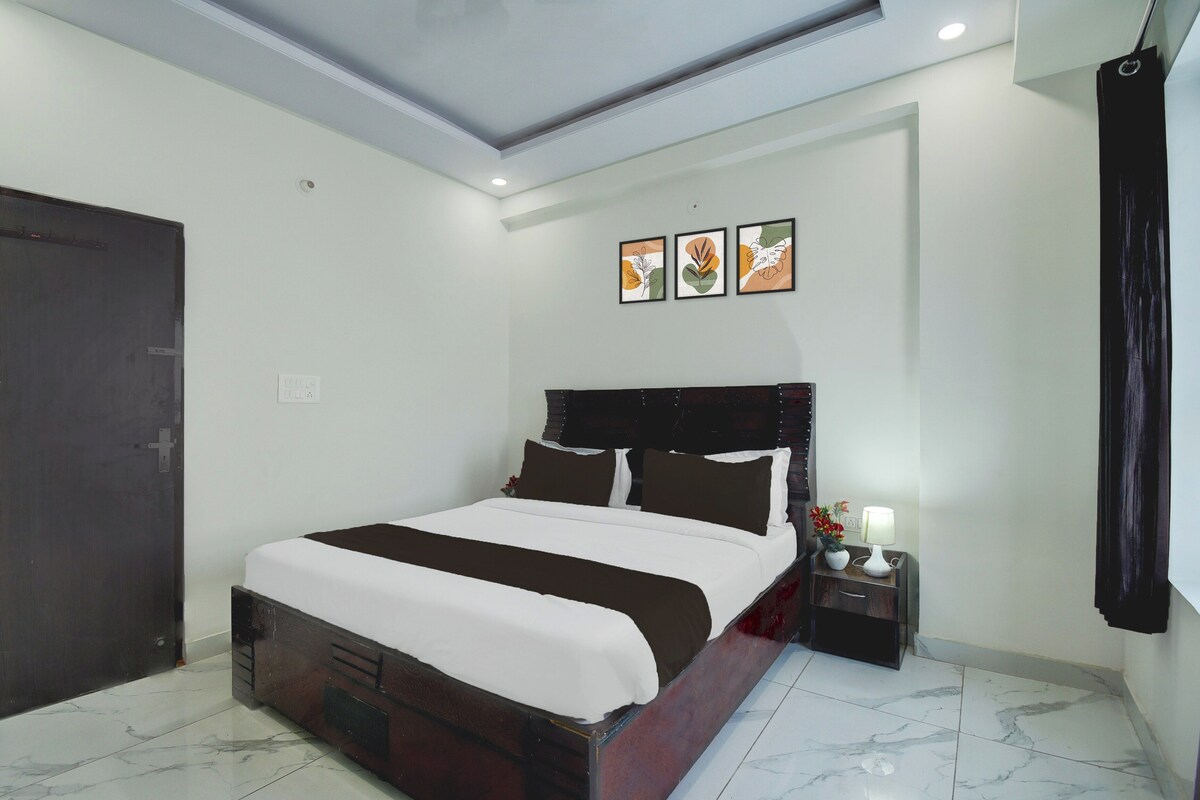 A hotel room with a large bed, a nightstand with a lamp, and a door.