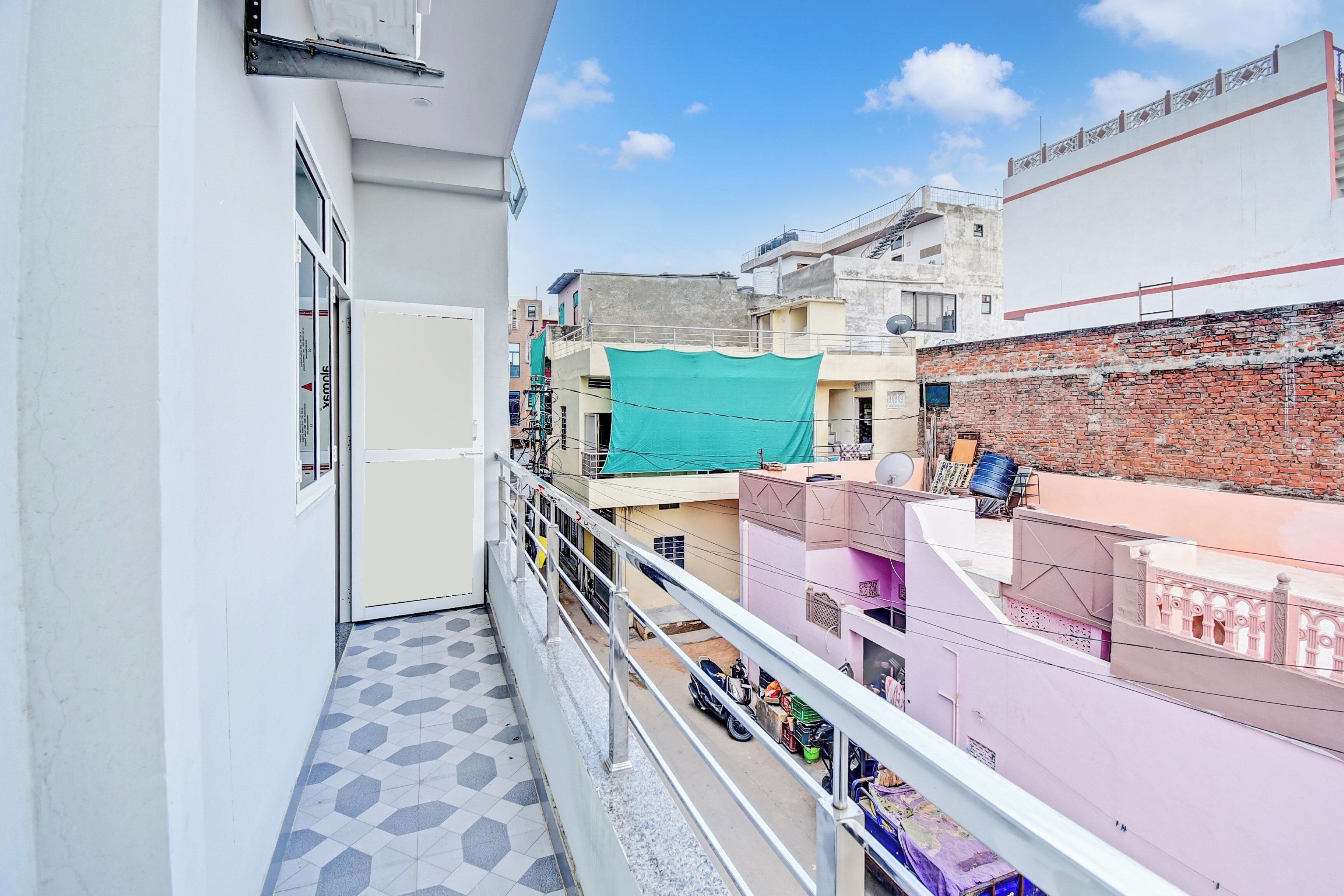 Un balcón estrecho con suelo de baldosas, baranda metálica y vistas a edificios cercanos.