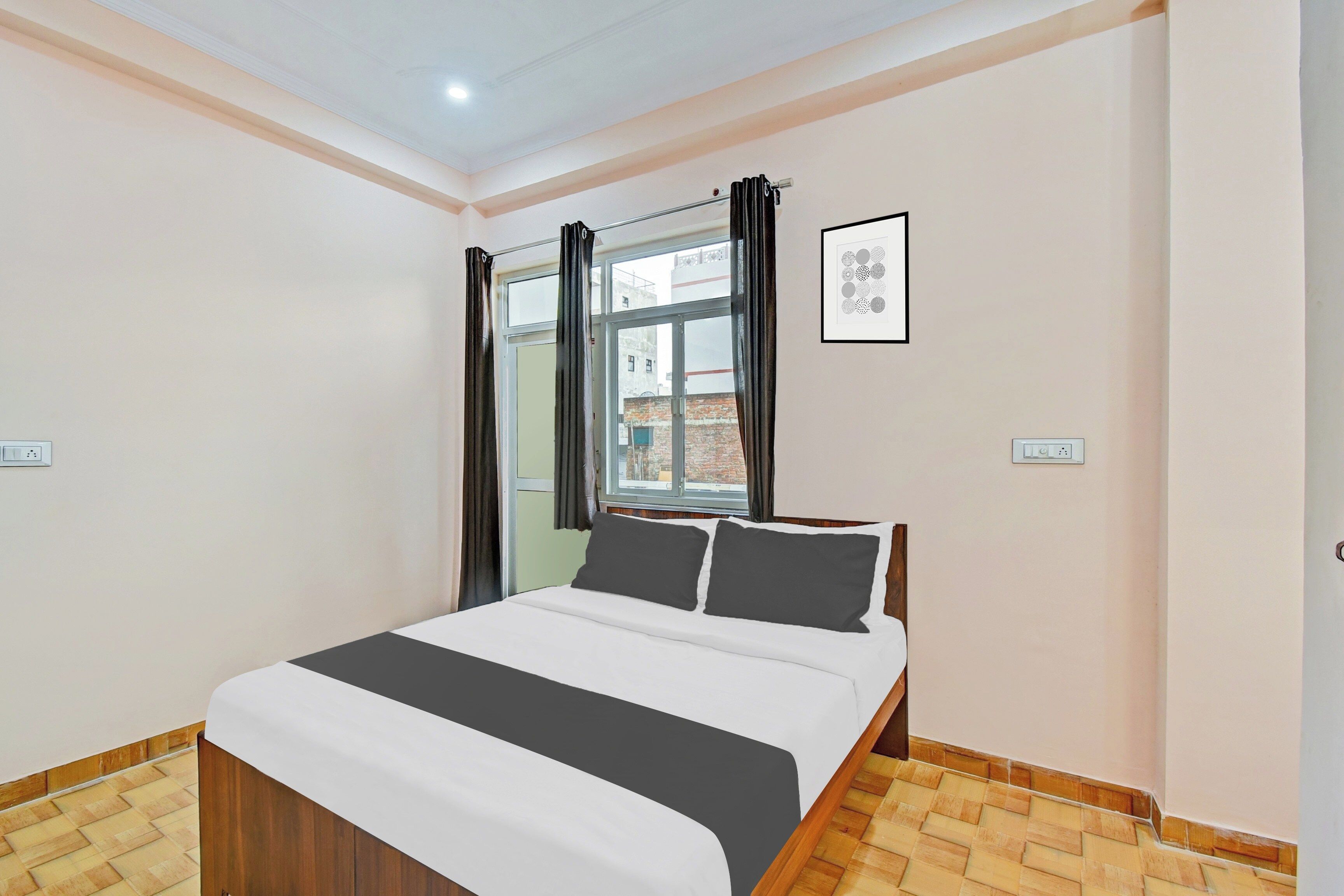 A bedroom with a bed, a window with curtains, a wall-mounted picture, and a light switch.