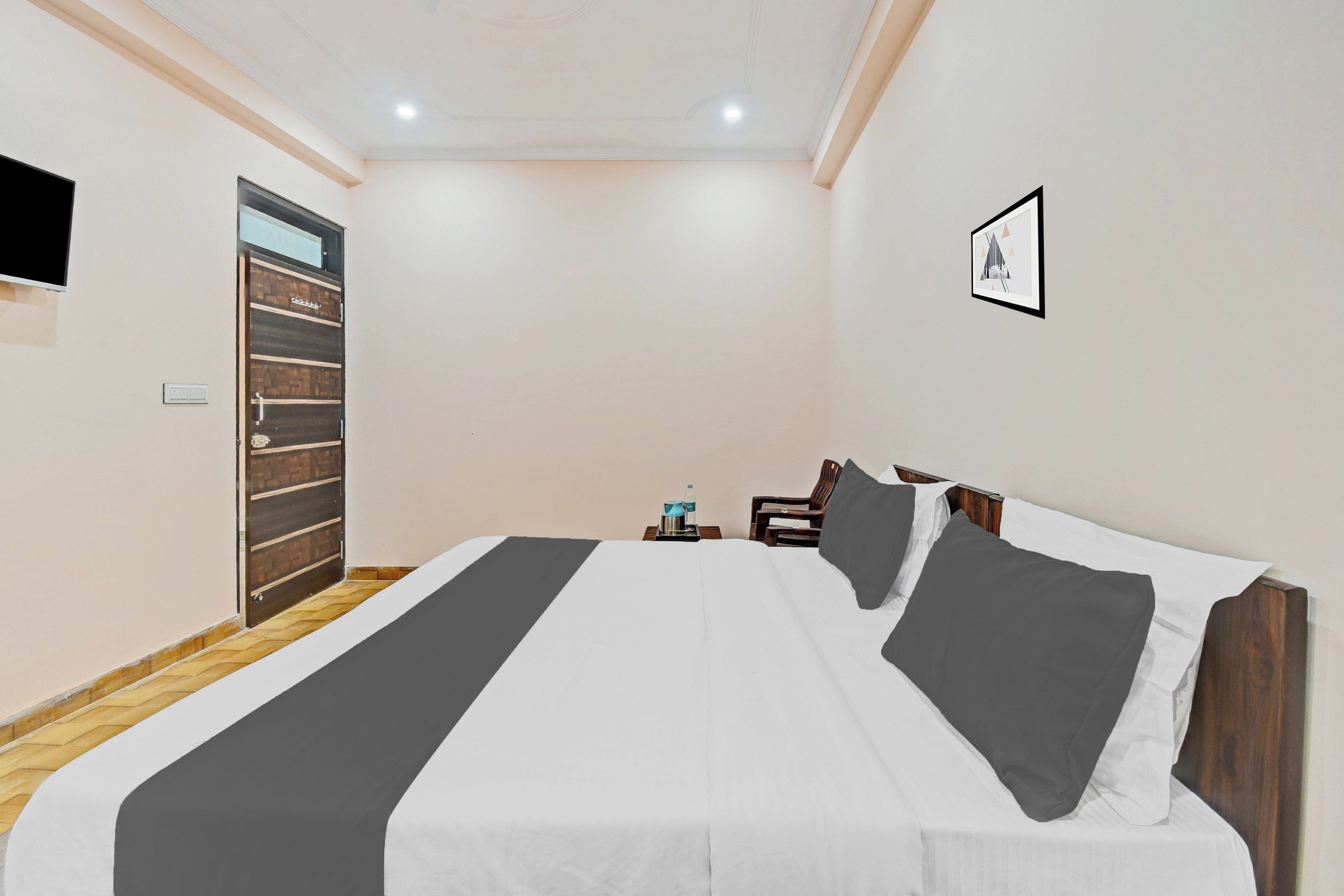 Habitación de hotel con cama, escritorio, silla, televisor montado en la pared y puerta.