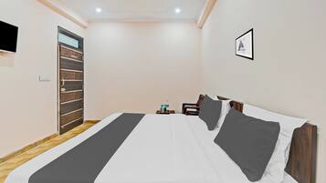 Habitación de hotel con cama, escritorio, silla, televisor montado en la pared y puerta.