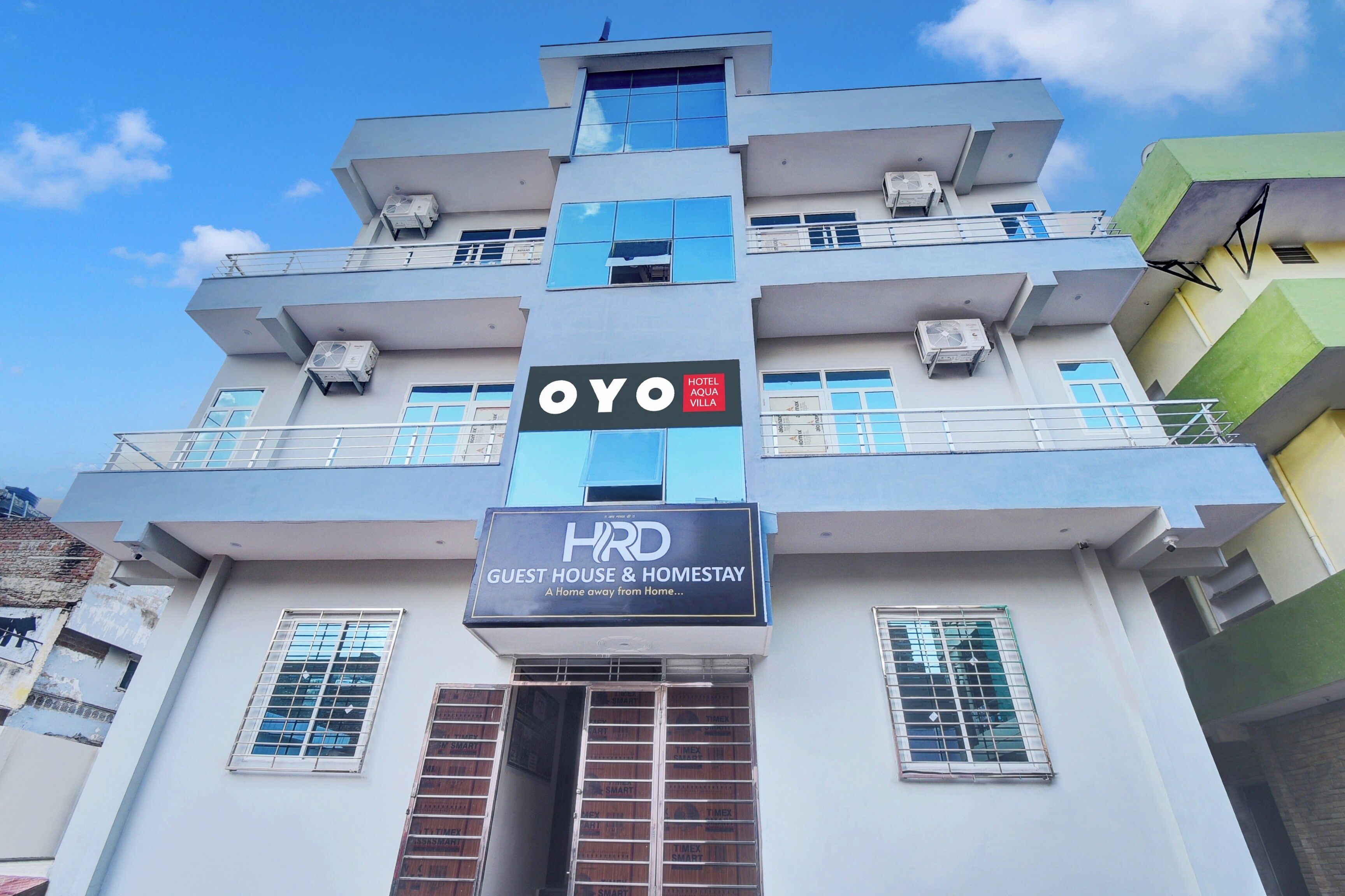 A multi-story building with a sign for 'OYO HOTEL AQUA MILLA' and 'HRD GUEST HOUSE & HOMESTAY'.