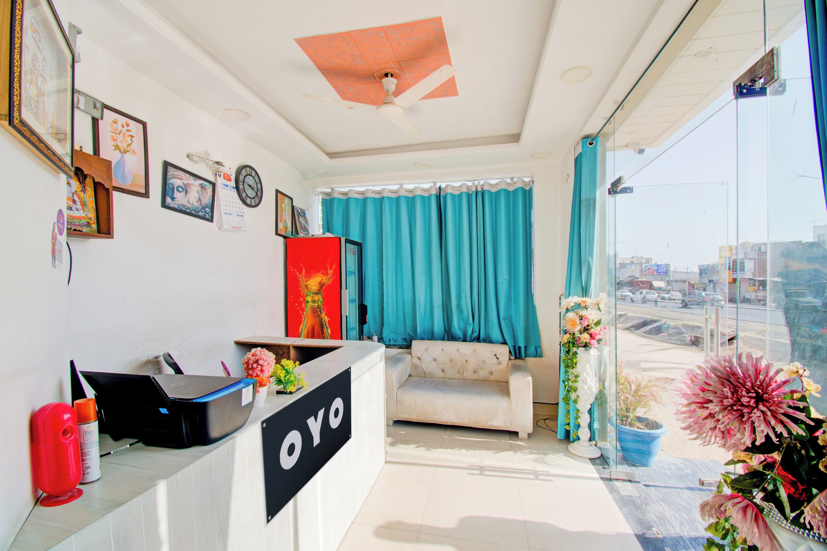 A room with a reception desk, a sofa, a ceiling fan, a window with curtains, and a view of the outside.