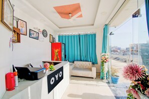 Ein Zimmer mit einer Rezeption, einer Couch, einem Deckenventilator, einem Fenster mit Vorhängen und Blick ins Freie.