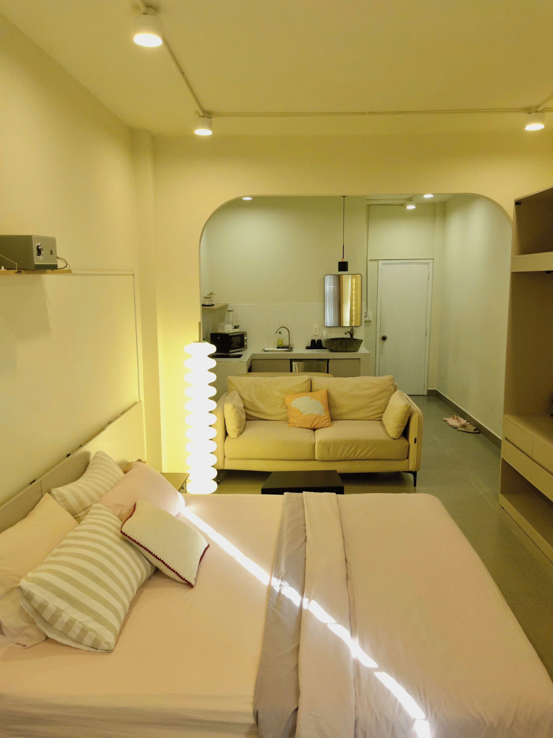 A compact hotel room with a bed, a sofa, a kitchenette, and a door leading to a bathroom.