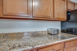 Eine Küche mit Holzschränken, einer Granitarbeitsplatte und einem schwarzen Kühlschrank.