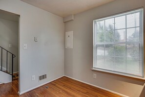 Ein Zimmer mit Holzboden, einem Fenster mit Jalousien, einer weißen Wand und einer Tür zu einer Treppe.