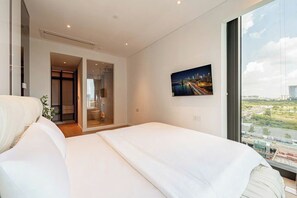A modern hotel room with a large bed, a cityscape view, and a sliding door leading to a bathroom. - The MetropoIe Urban Residence Sai Gon  (An Khanh)