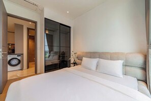 A modern hotel room with a large bed, a washing machine, and a sliding glass door leading to a bathroom. - The MetropoIe Urban Residence Sai Gon  (An Khanh)