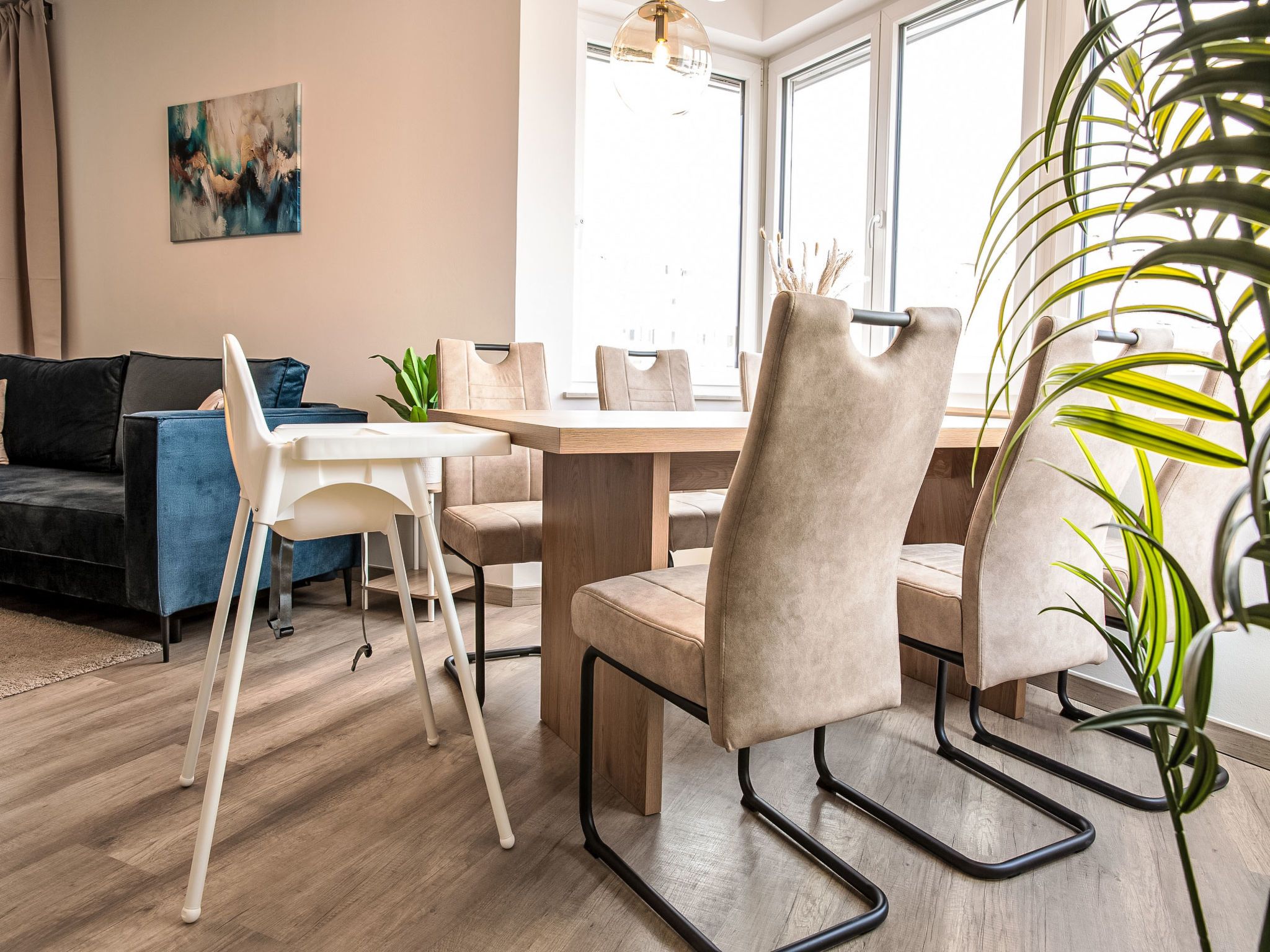 Ein modernes Wohnzimmer mit einer Couch, einem Esstisch und Stühlen. An der Wand hängt ein Gemälde und in der Ecke steht eine Pflanze.