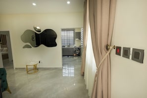 Une chambre d’hôtel avec un sol en marbre, une table ronde et une chaise blanche, une horloge murale, un téléviseur à écran plat, un lave-linge et une porte dotée d’une serrure de sécurité.