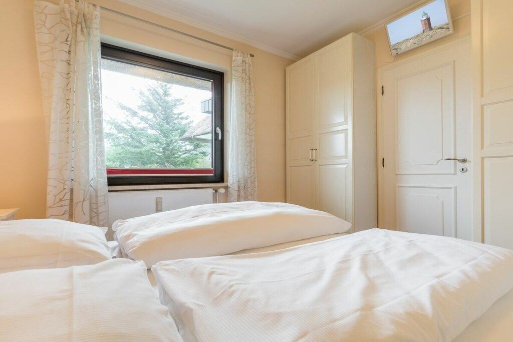 Een slaapkamer met twee bedden, een raam met gordijnen en een televisie aan de muur.