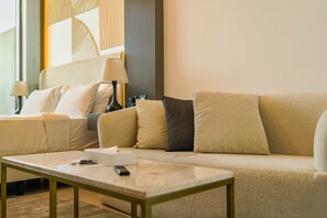 A hotel room with a sofa, a bedside table with a remote control, and a lamp. - HAVN - Studio in Prime Residency, Al Furjan (Dubai)