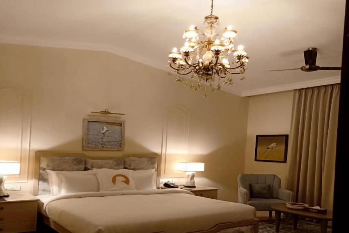 Una habitación de hotel con una cama grande, un candelabro, un reloj, una silla y una mesita.