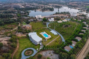 Vista aérea de un complejo turístico con piscina, casas de huéspedes y una extensa masa de agua.