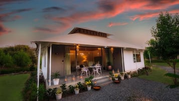 Una casa moderna con un patio cubierto, mobiliario exterior y plantas en macetas.