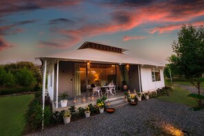 Una casa moderna con un patio cubierto, mobiliario exterior y plantas en macetas.