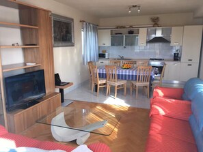 Un espacio habitable compacto con televisor, sofá, mesa de comedor y zona de cocina.