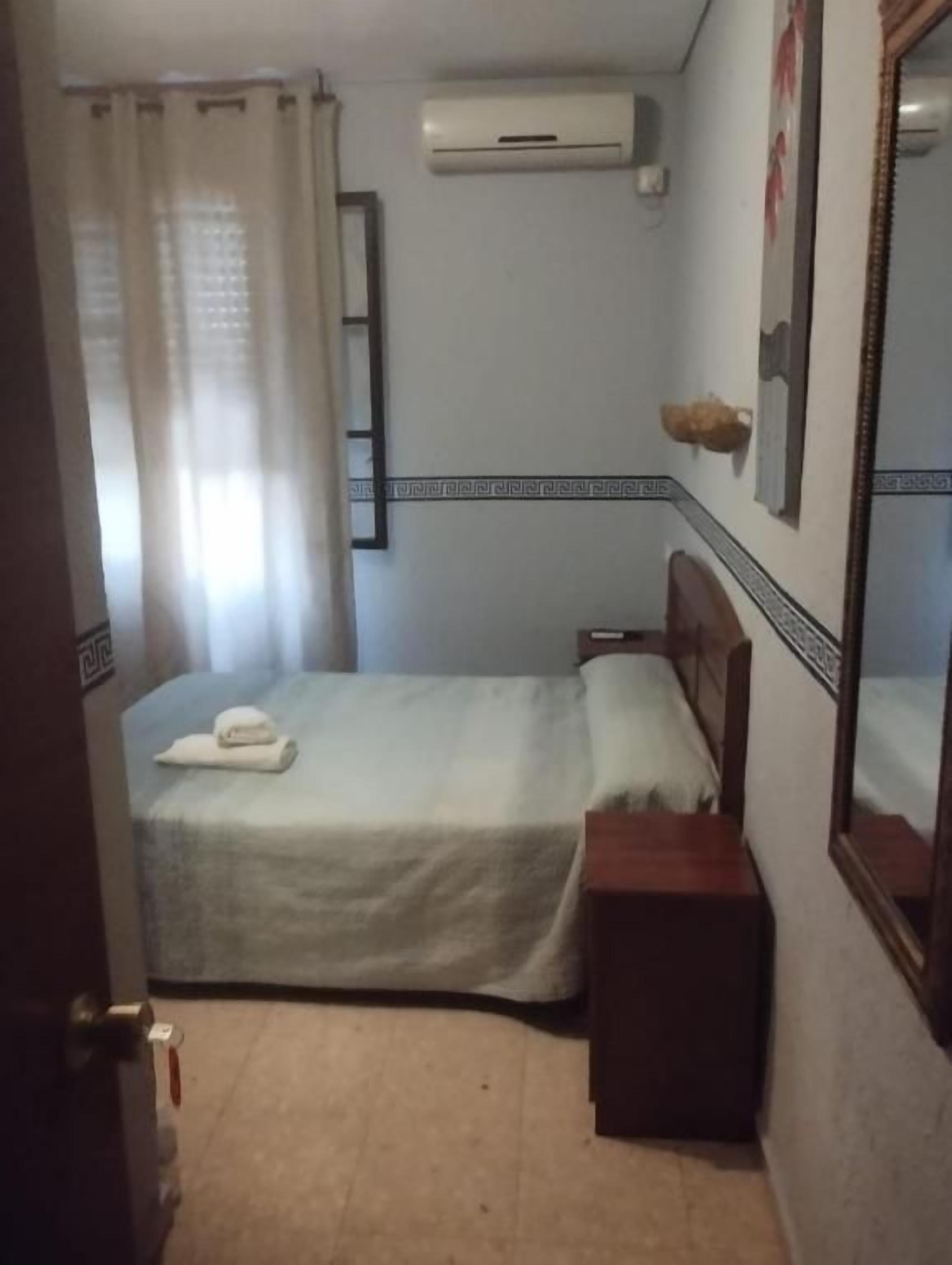 Una habitación pequeña con una cama individual, cabecera de madera, mesita de noche y un espejo.