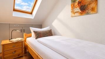 Ein Schlafzimmer mit Dachfenster, einem Bett mit weißer Bettwäsche, einem Nachttisch mit Lampe, einer Holzkassette und einem Wandregal.