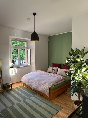 Ein Schlafzimmer mit einem Bett, einem Fenster, einer Pflanze und einem kleinen Tisch.