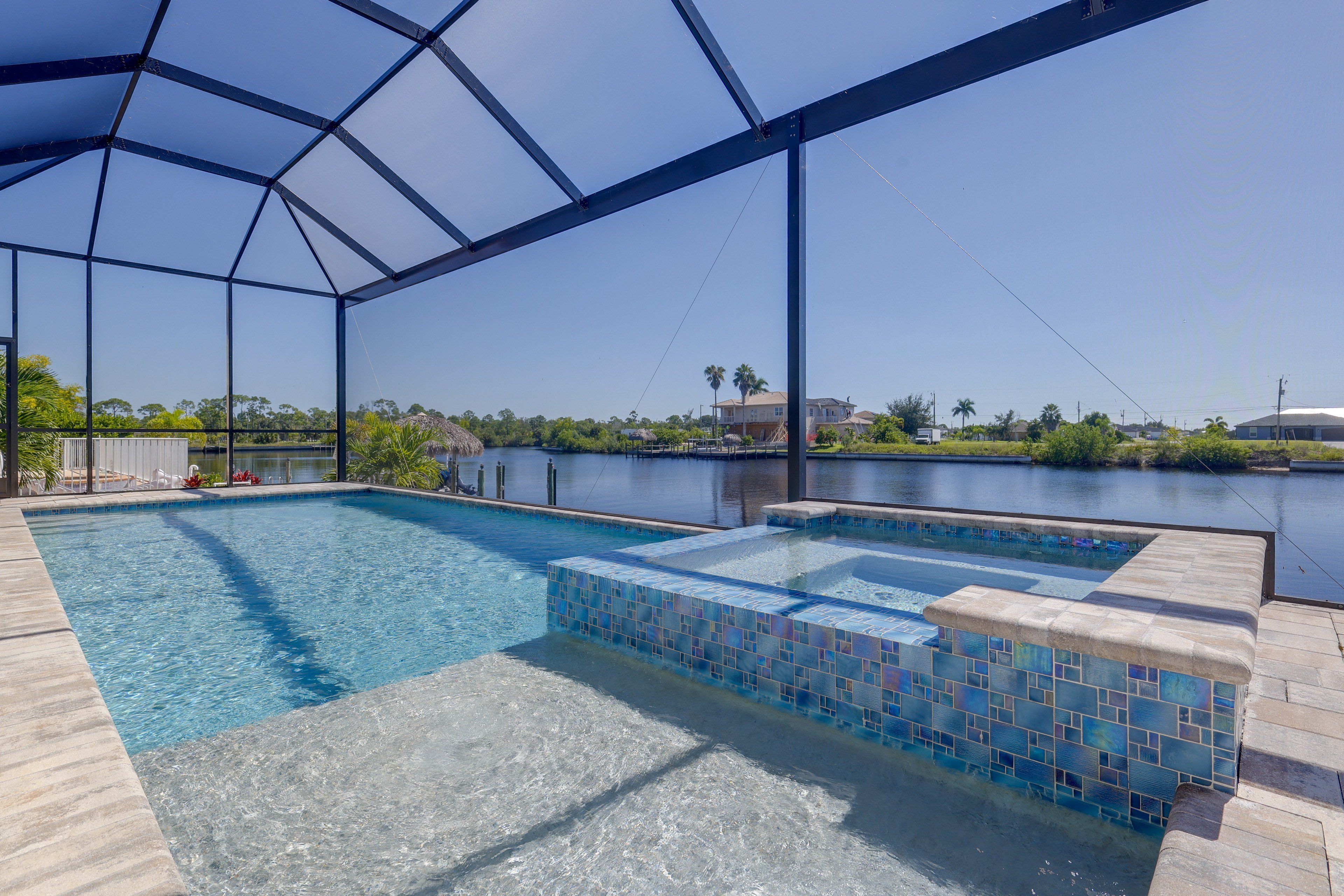 A swimming pool with a glass enclosure, a hot tub, and a view of a body of water and greenery.