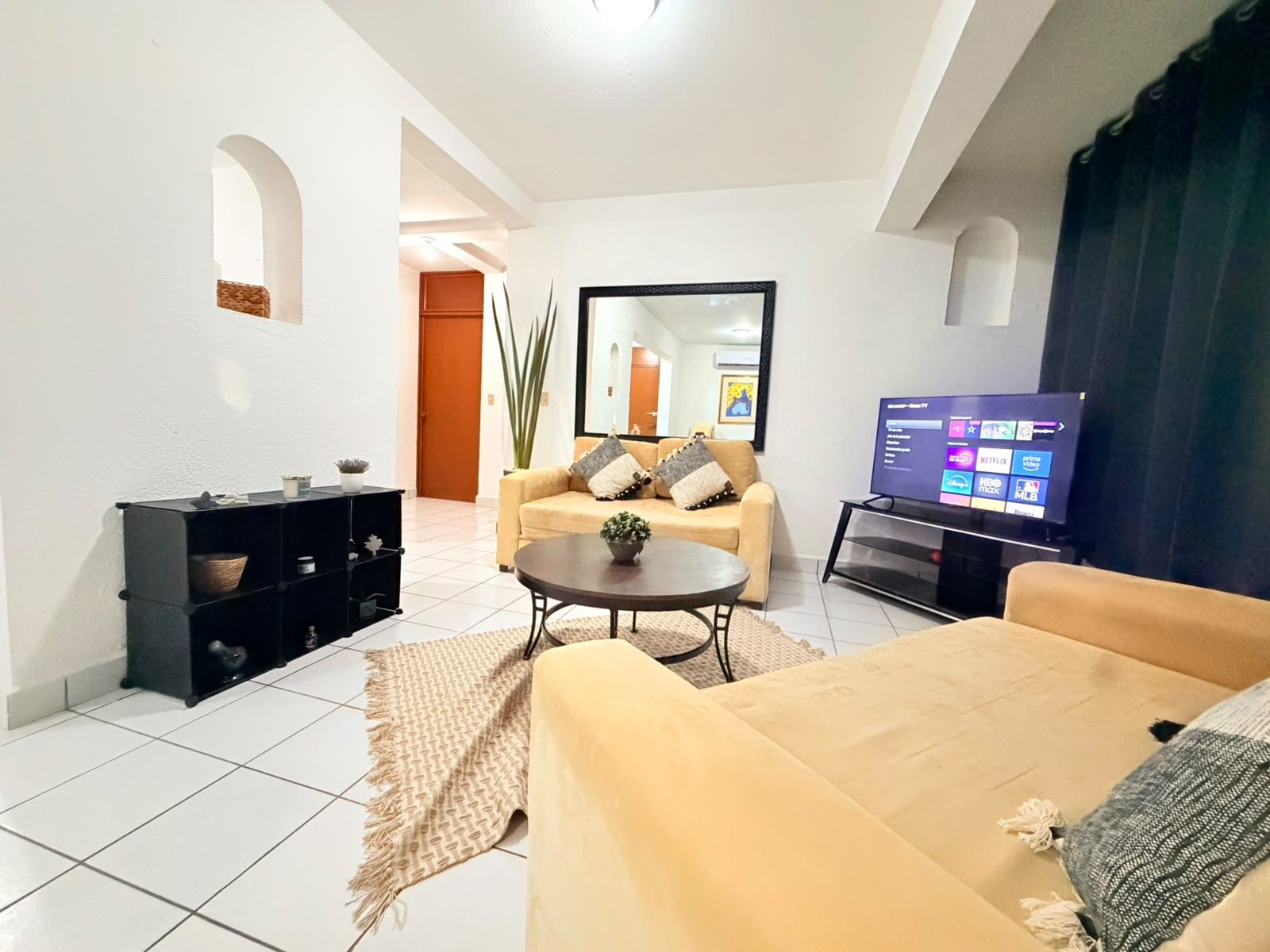 A modern living room with a sofa, coffee table, and TV. There is a black entertainment unit and a plant.