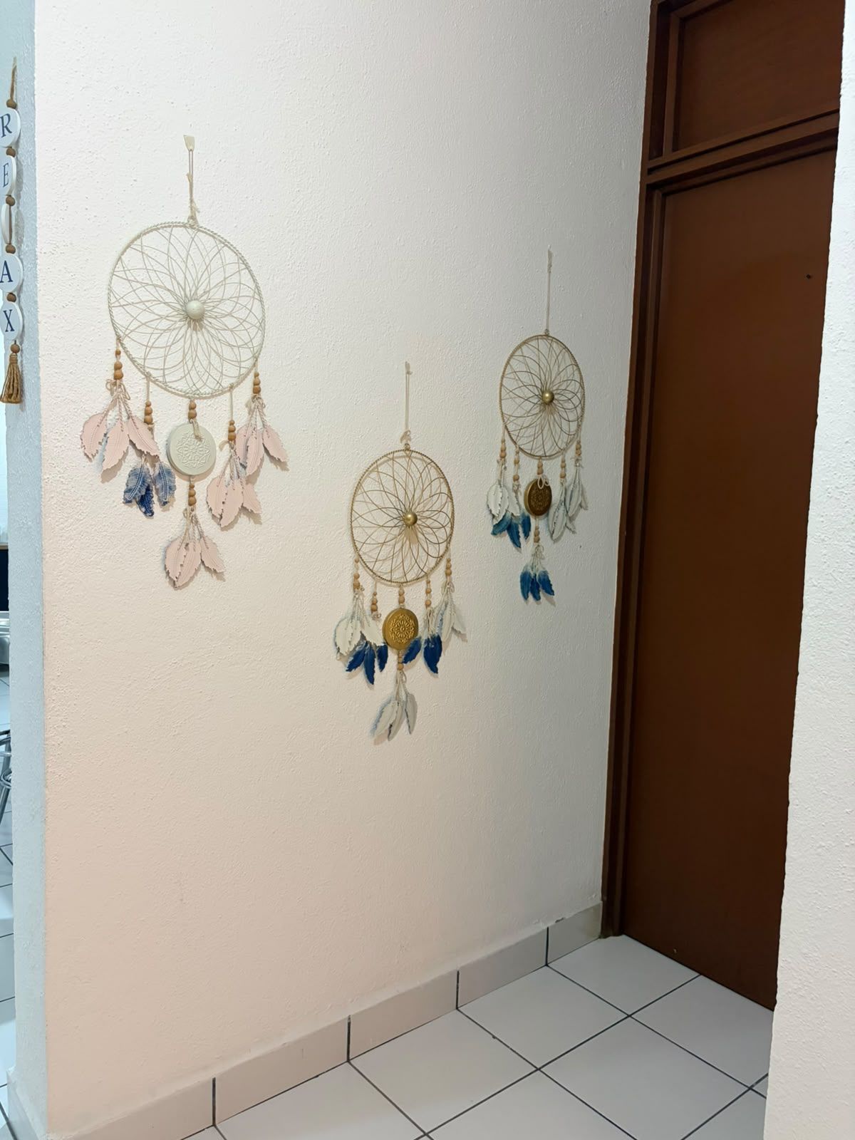 A wall with three dreamcatchers hanging, a brown door, and a tiled floor.