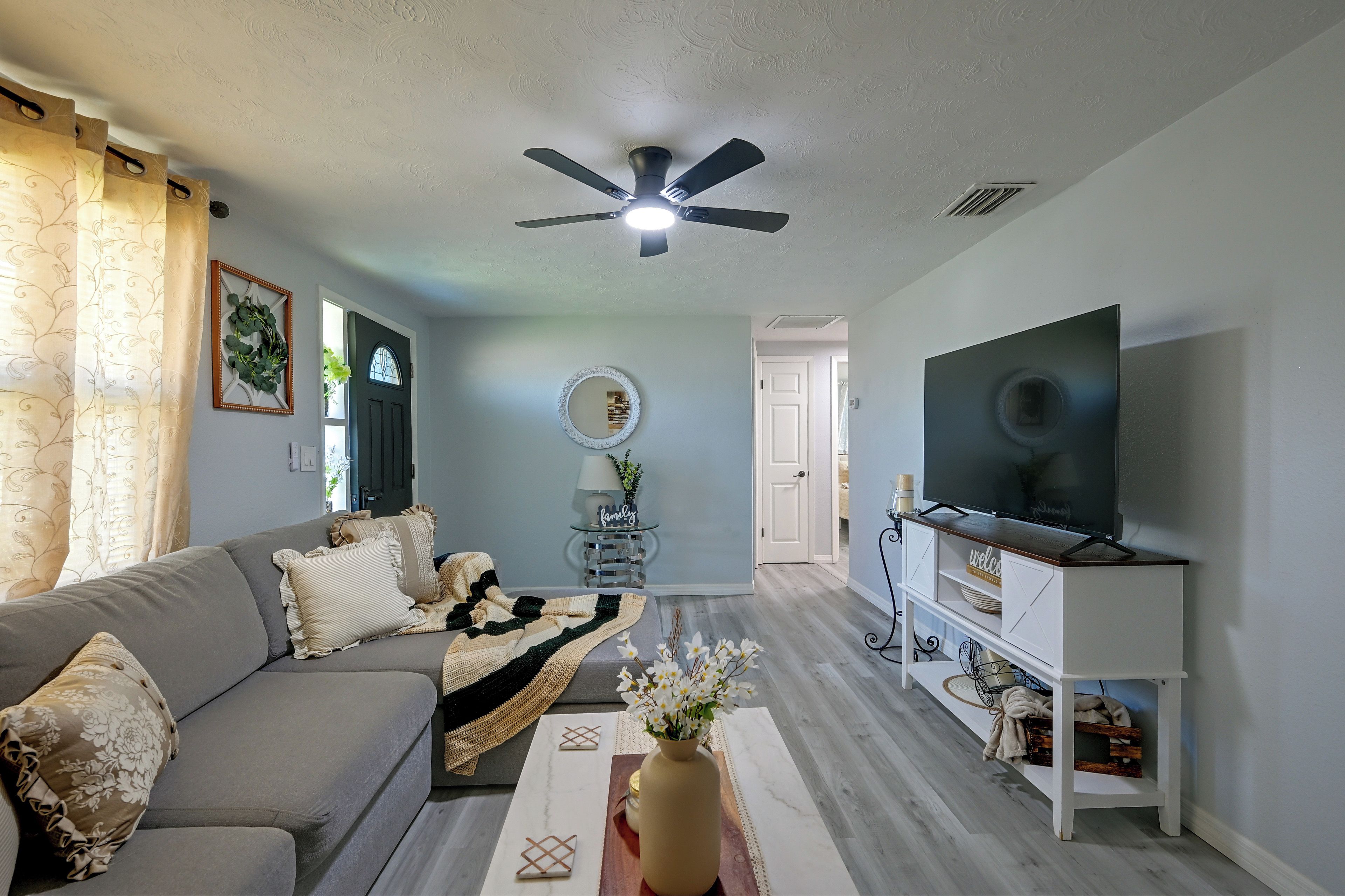 Un salon comprenant un canapé, un téléviseur, un ventilateur de plafond et un miroir décoratif.