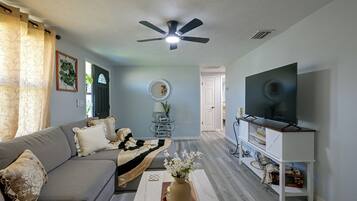 Un salon comprenant un canapé, un téléviseur, un ventilateur de plafond et un miroir décoratif.