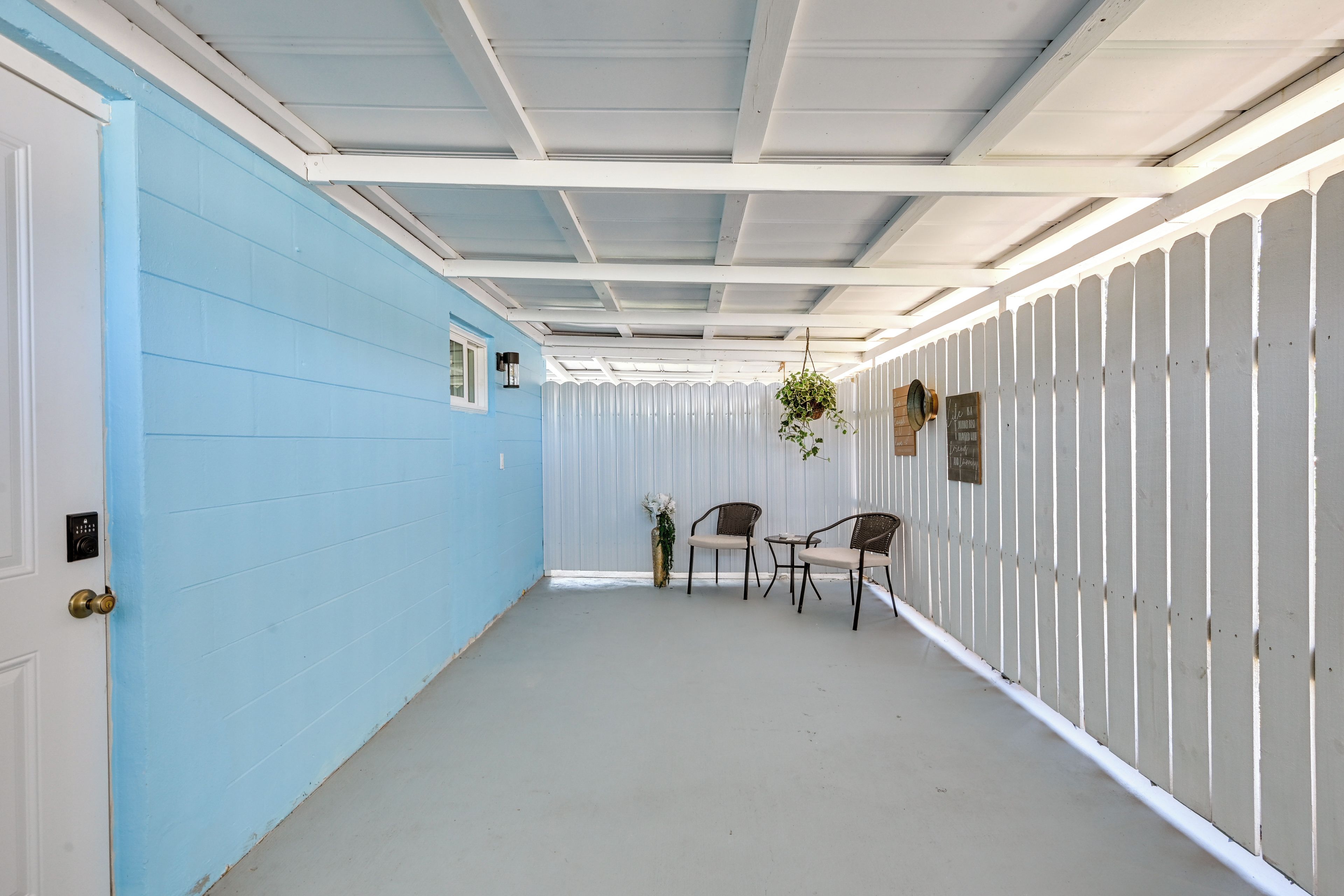Um corredor com uma parede azul de um lado e uma parede branca do outro, que leva a um espaço de estar com duas cadeiras e uma mesa.