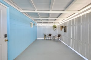 Um corredor com uma parede azul de um lado e uma parede branca do outro, que leva a um espaço de estar com duas cadeiras e uma mesa.