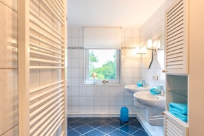 Ein Badezimmer mit Fenster, zwei Waschbecken und einer blauen Toilette.
